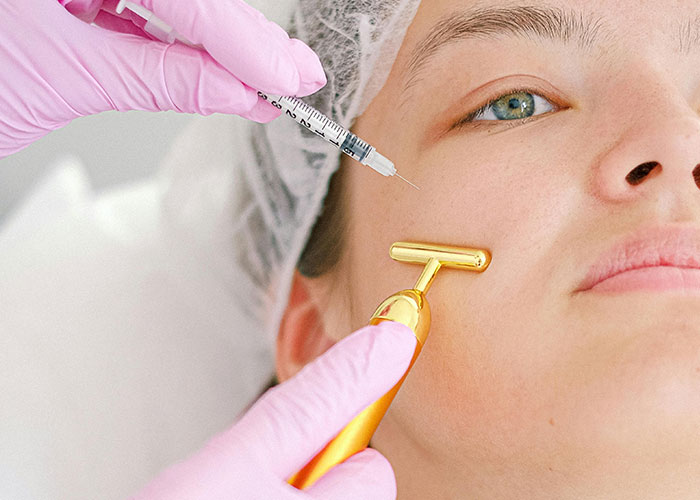 Close-up of a person receiving a facial injection and using a gold facial roller, highlighting social norms people hate the most.